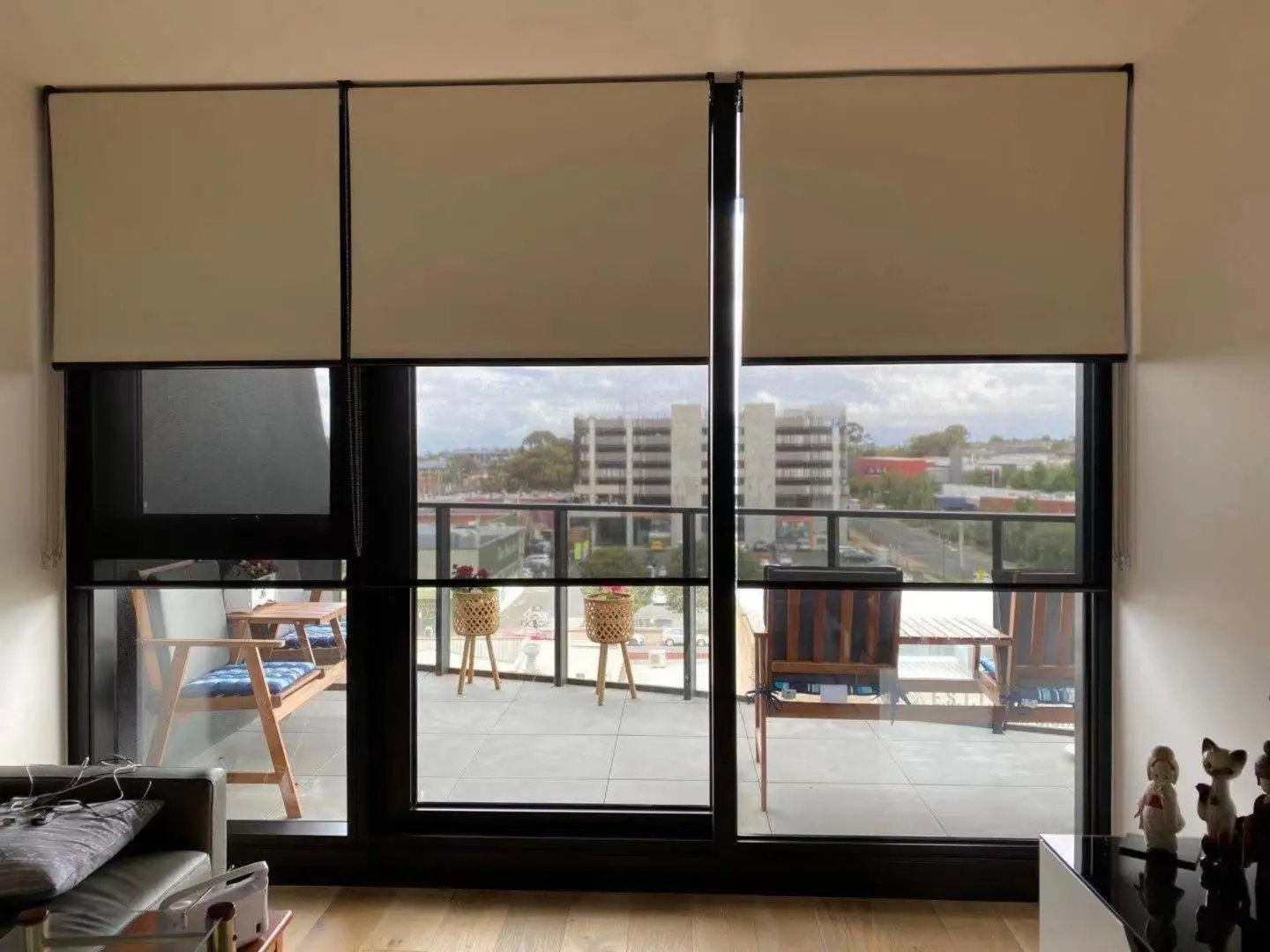 Modern apartment window with beige roller blinds and a balcony city view.