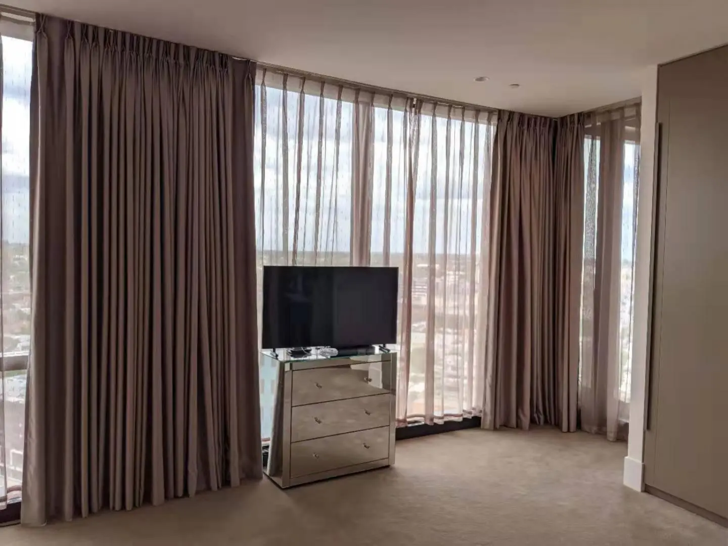 Brown curtains frame a modern living room window with a TV stand.