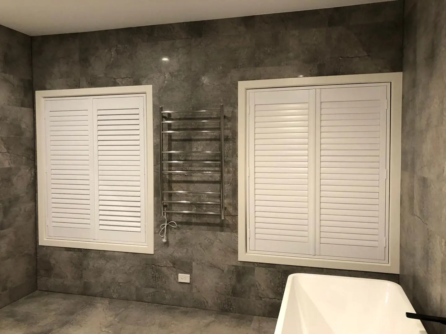 Stylish bathroom features white shutters, a heated towel rack, and a modern soaking tub.