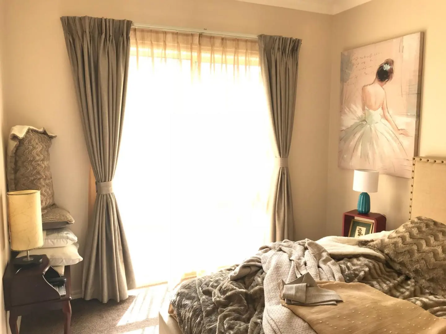 Bedroom interior with curtains, artwork, and cozy bedding.