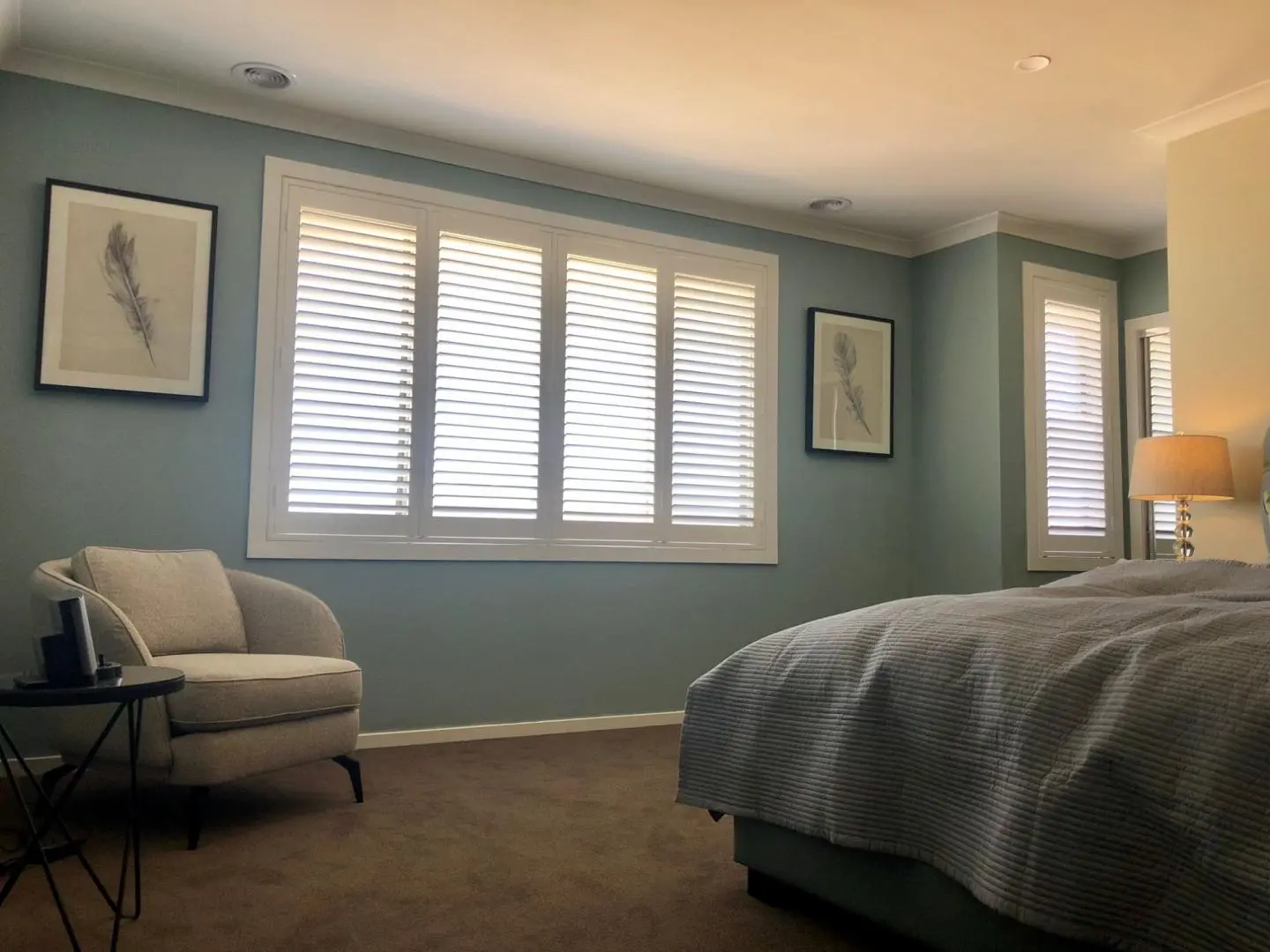Stylish bedroom interior featuring shutter blinds, artwork, and a cozy armchair.