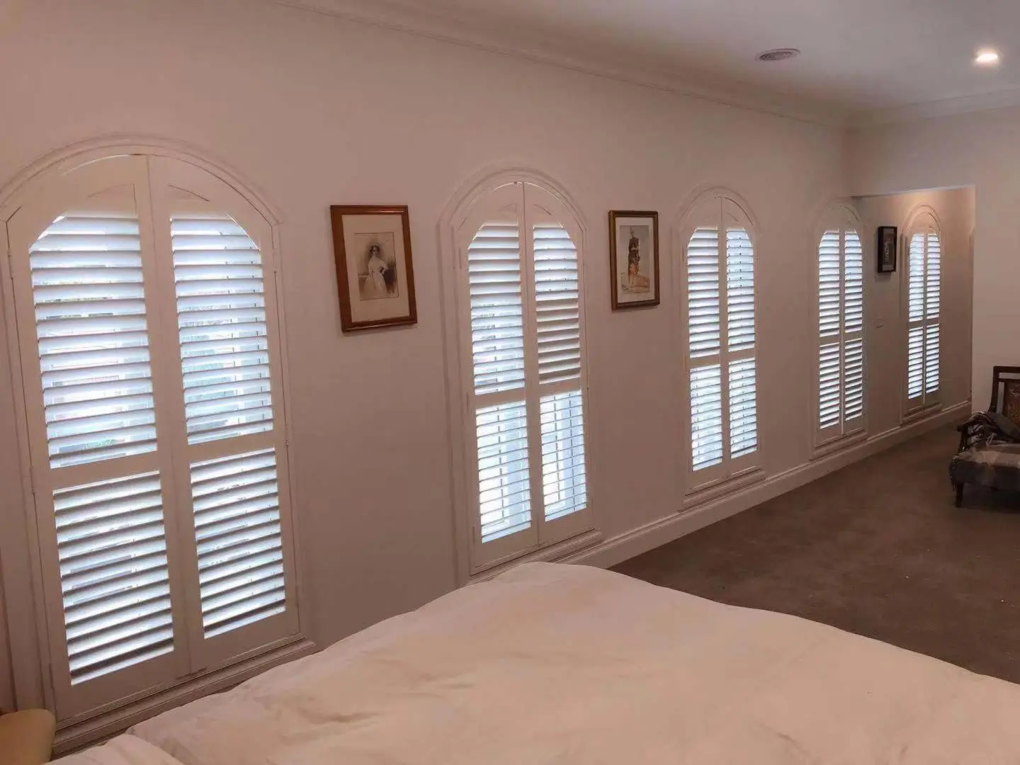 A bright bedroom features arched shutters, framed pictures, and a cozy atmosphere.