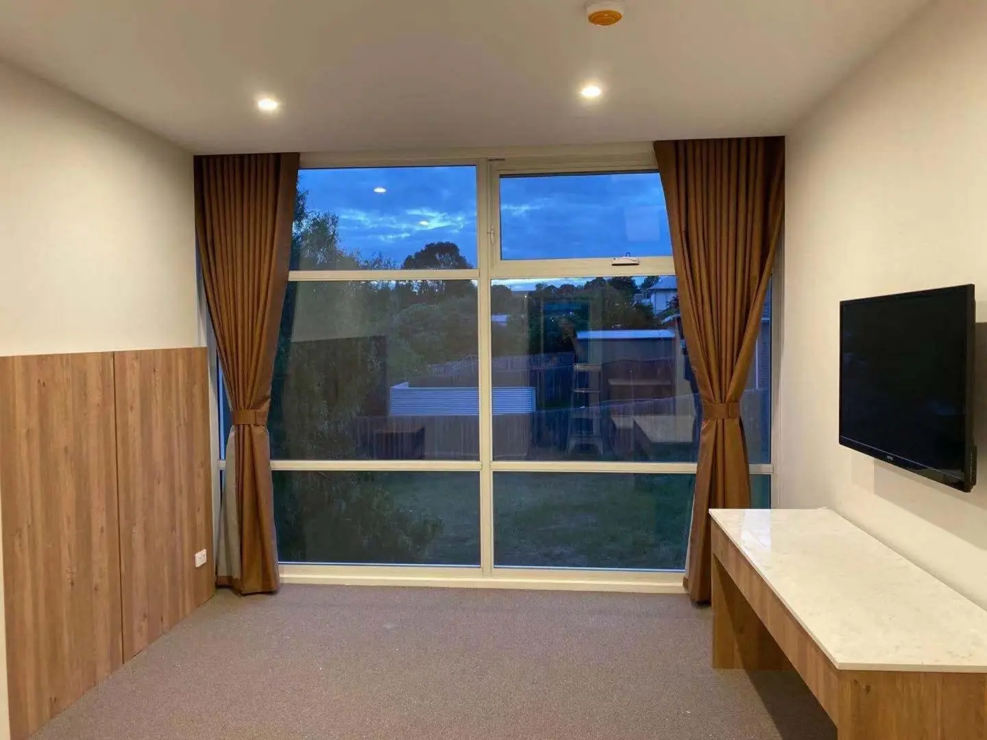 Bedroom with brown curtains framing a window and a TV.