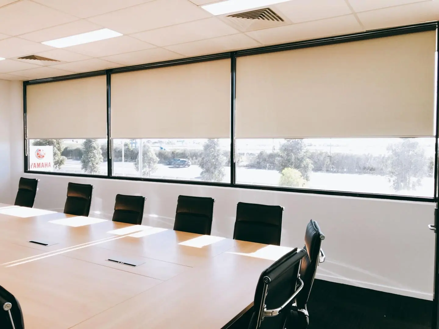 Modern conference room with beige roller blinds on large windows and a long meeting table.