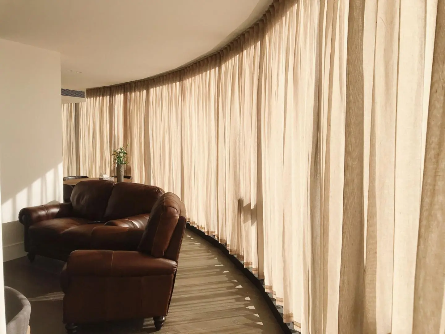 Beige curtains elegantly line a curved living room wall, enhancing aesthetics and controlling light.