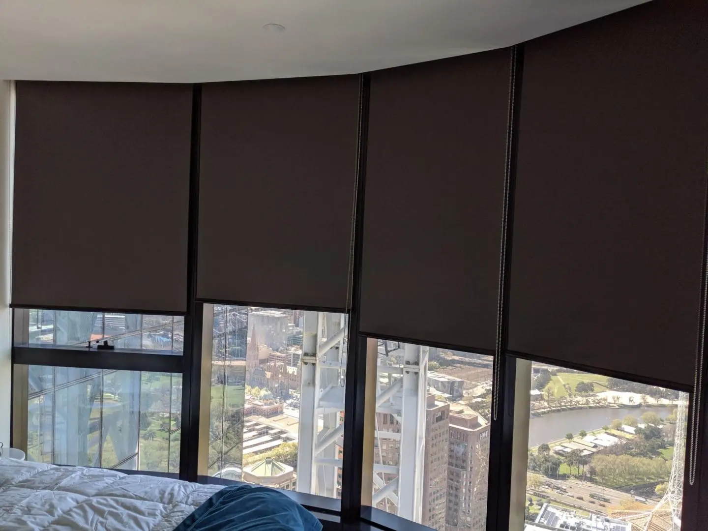 Partially drawn dark roller blinds in a bedroom overlooking a city and river.