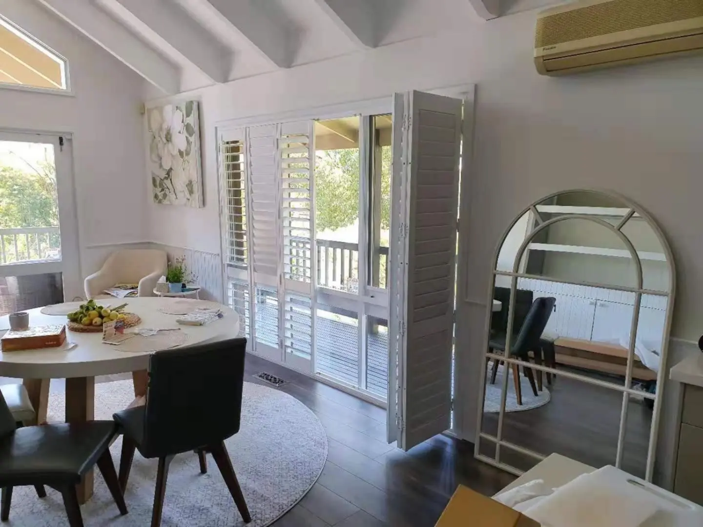 Bright dining room with shutter windows and an arched mirror, creating a modern aesthetic.