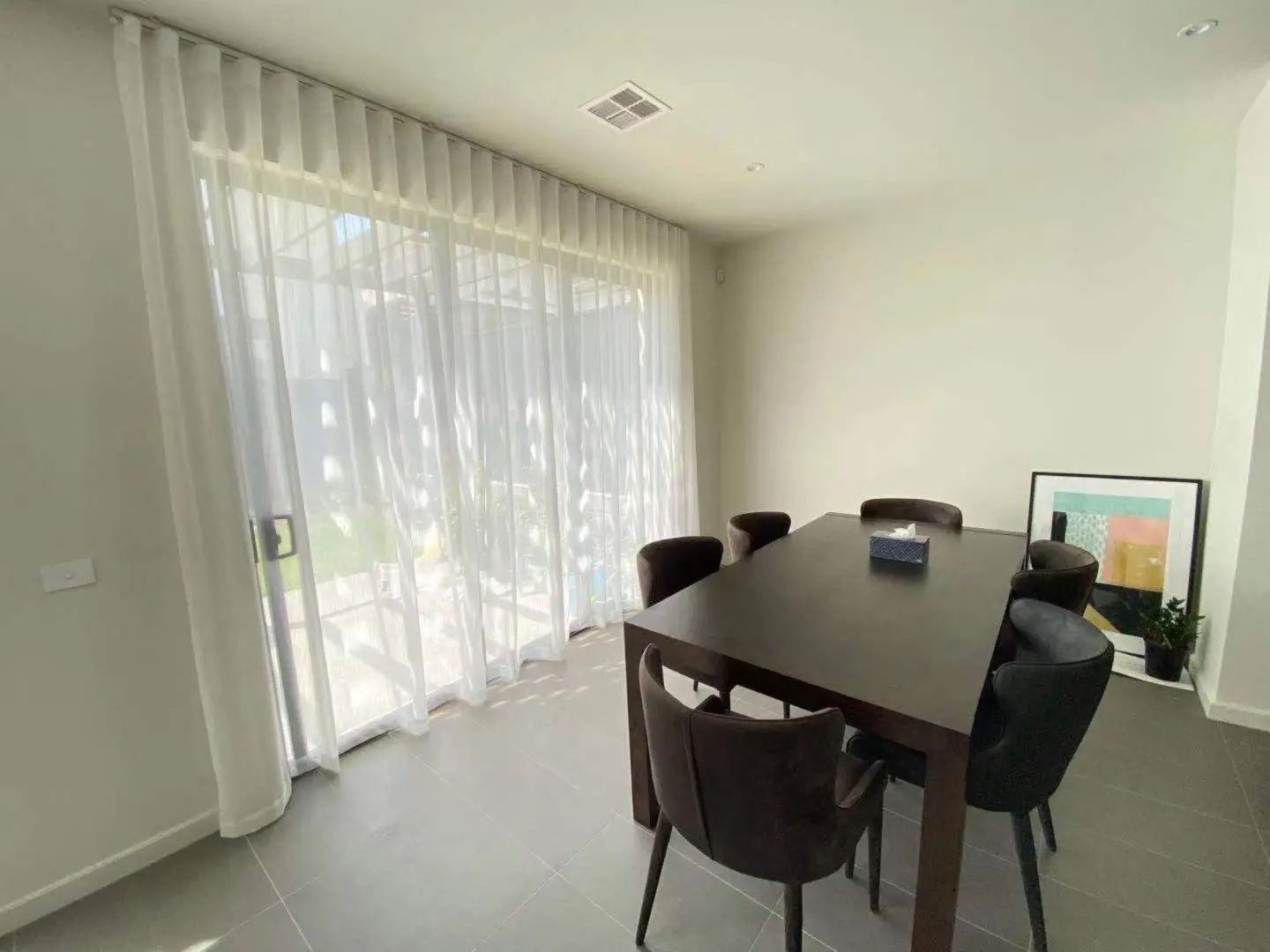 A modern dining room with a dark wood table, velvet chairs, and sheer curtains.