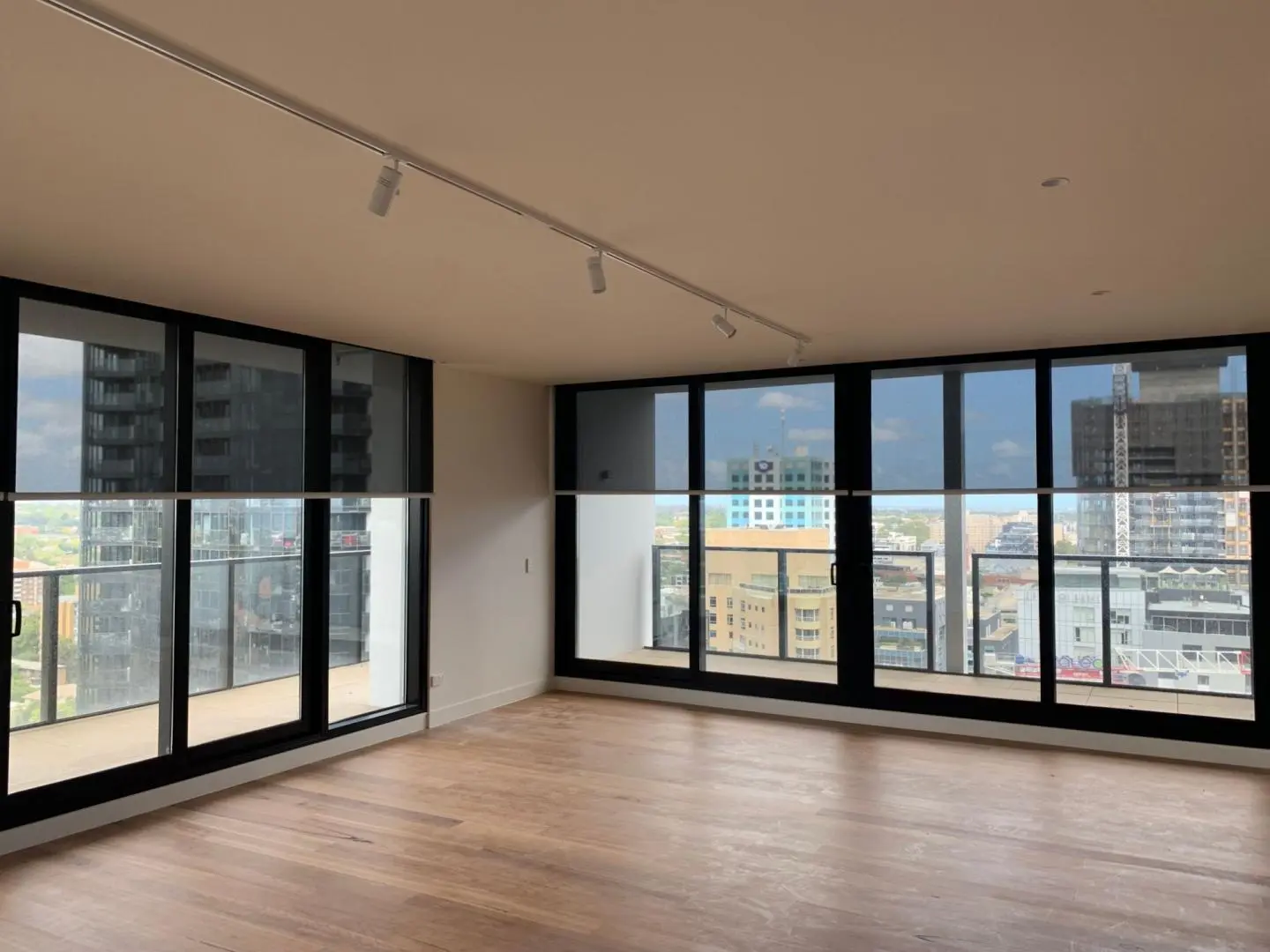 Empty modern apartment with city views and roller blinds on large windows.