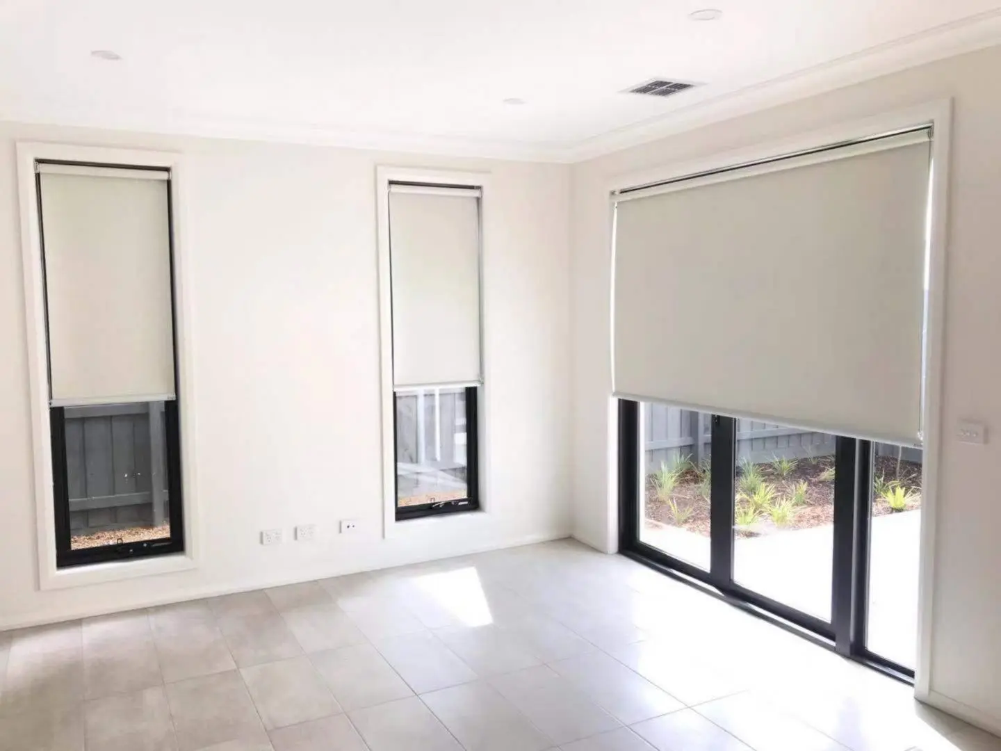 Bright empty room featuring white walls, a tiled floor, and windows with neutral roller blinds.