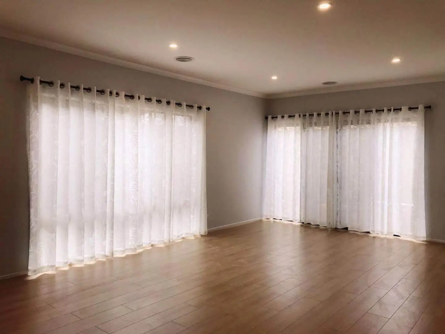 Empty room with sheer curtains and hardwood floors bathed in natural light.