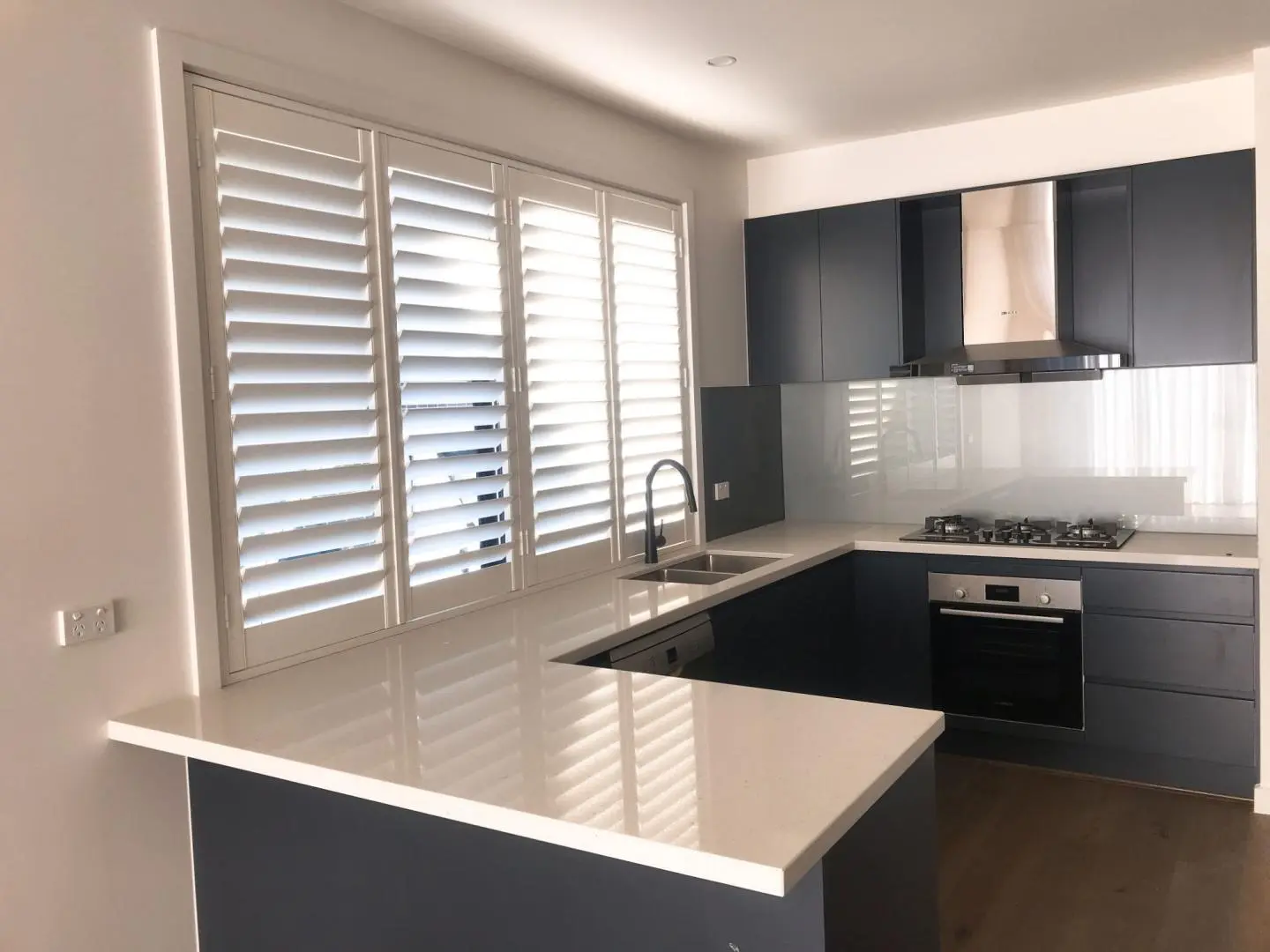 Stylish modern kitchen with dark cabinets, white countertops, and shuttered windows.