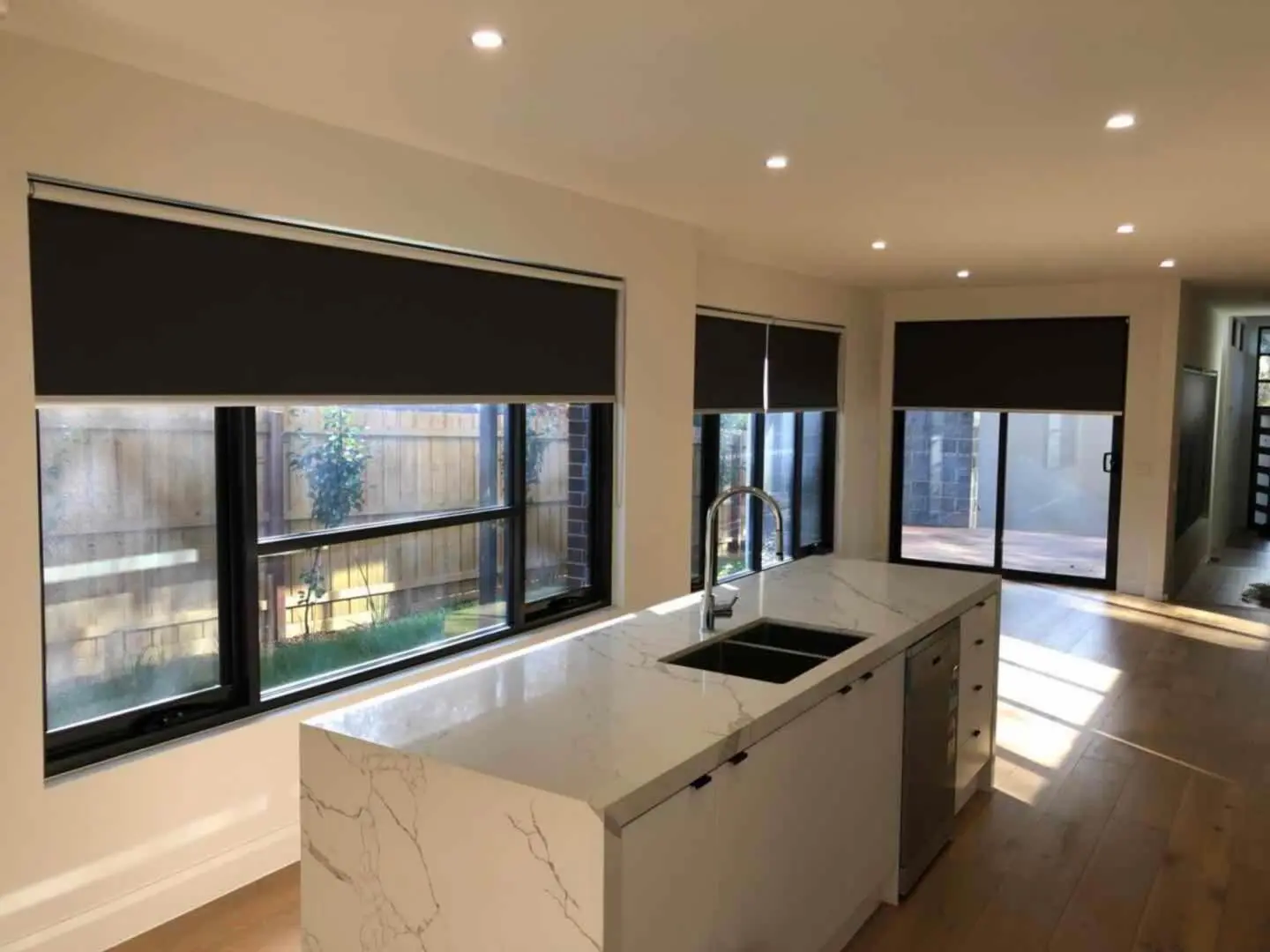 Black roller blinds cover the large windows and sliding doors in a modern kitchen.