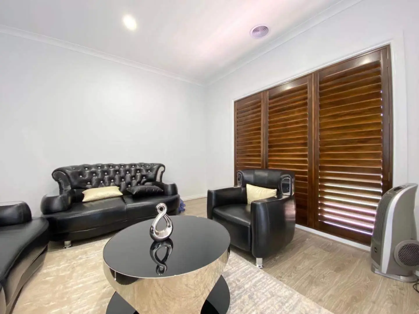 A stylish living room boasts dark leather furniture, a modern coffee table, and wooden shutters.