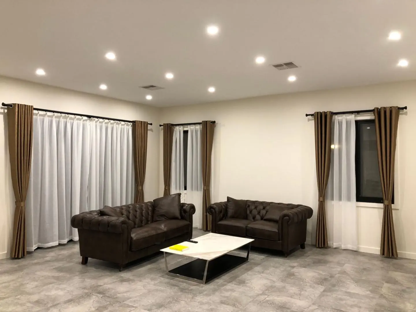 A living room features two leather sofas and brown and white curtains.