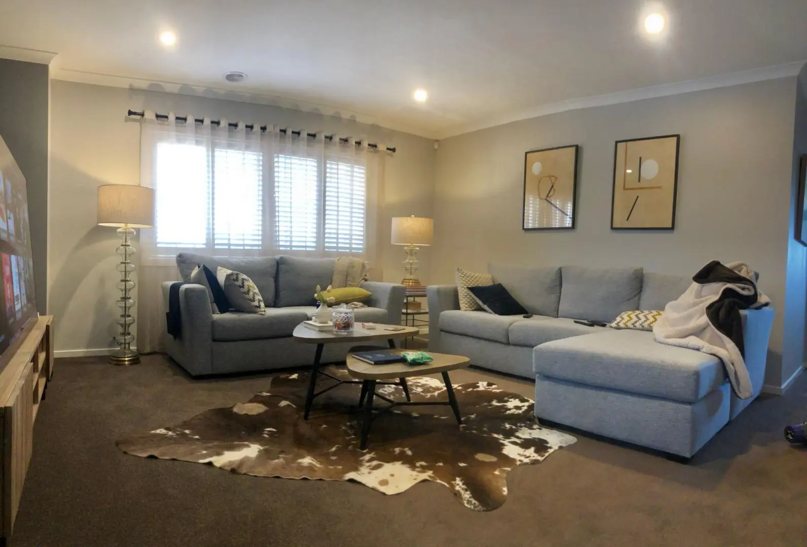 Cozy living room with light gray sofas, a stylish cowhide rug, and warm lighting.