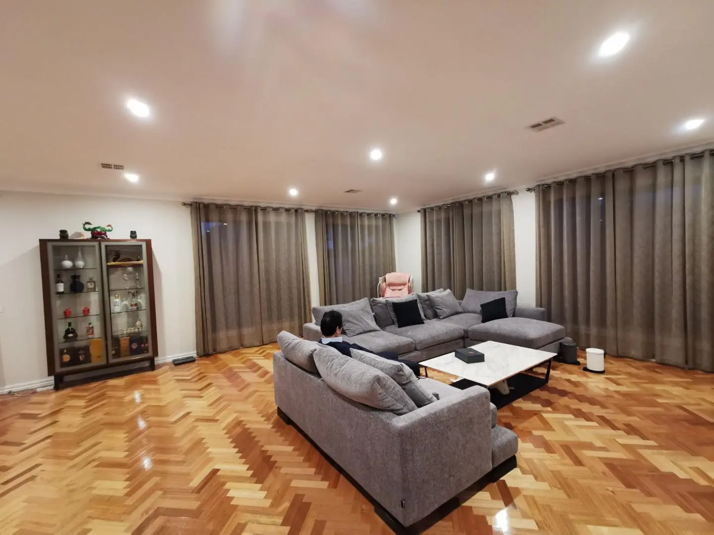 Spacious living room design with gray couches, brown curtains, and herringbone wood floors.