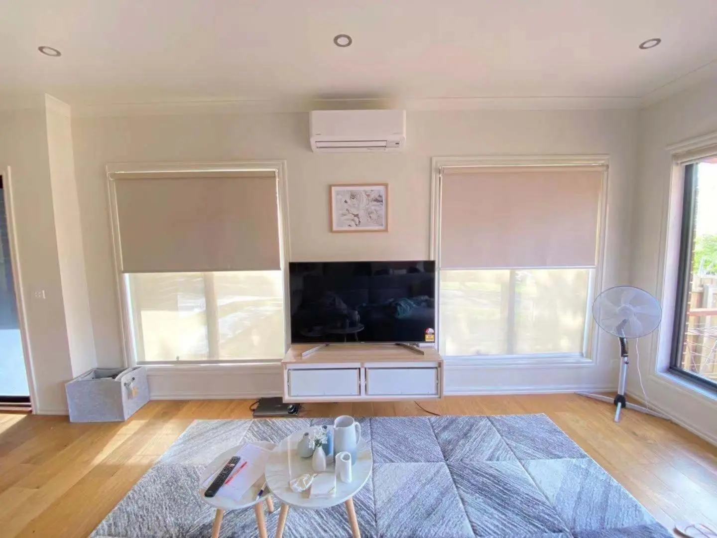 A bright modern living room with a TV, roller blinds, and a patterned rug.