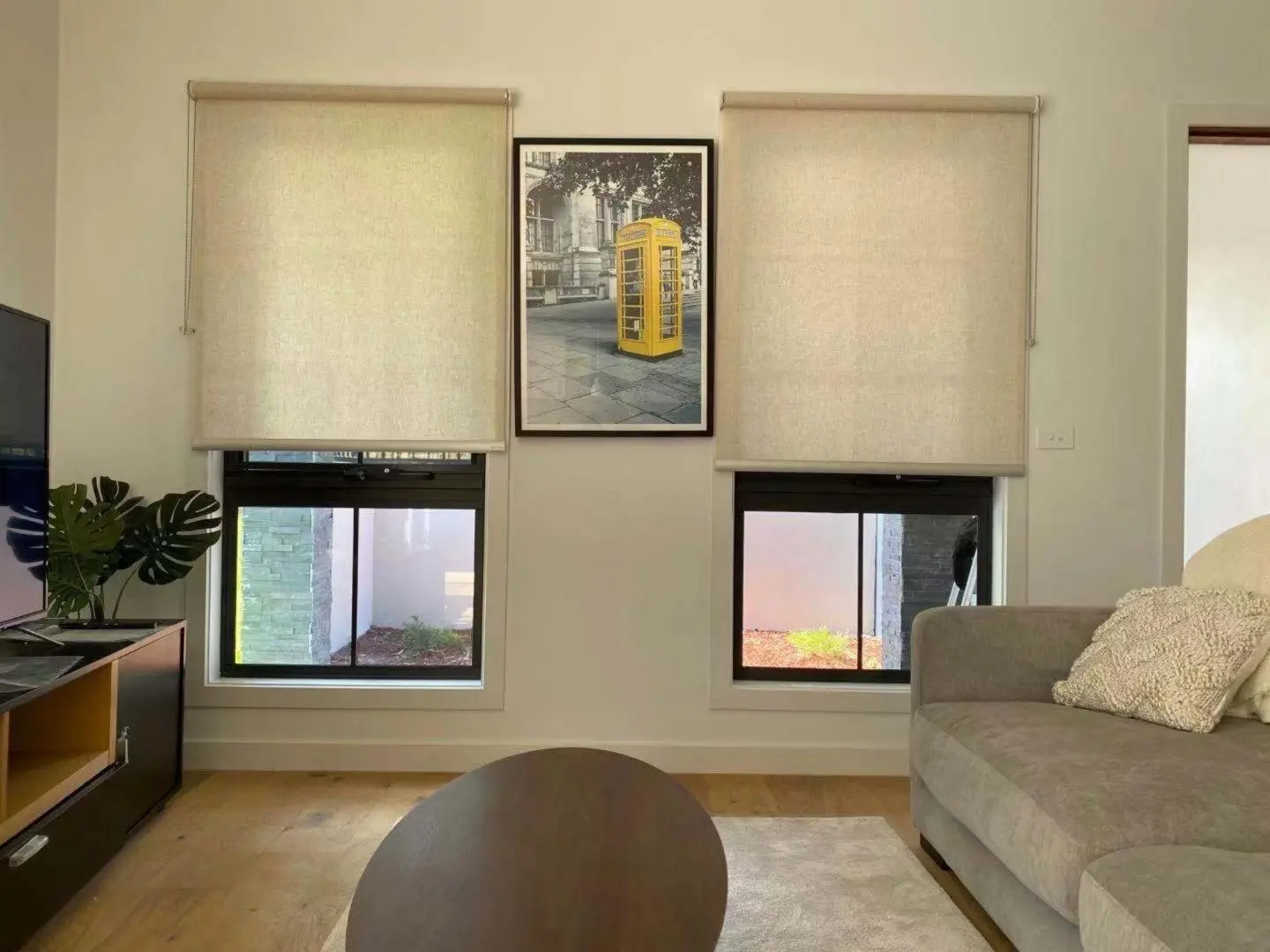 Beige roller blinds cover two windows in a modern living room.