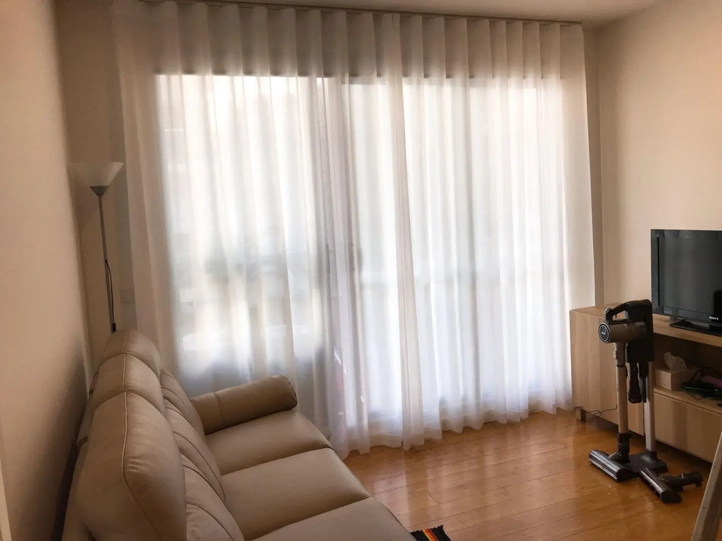 Cozy living room with sheer curtains, a couch, TV, and hardwood floors.