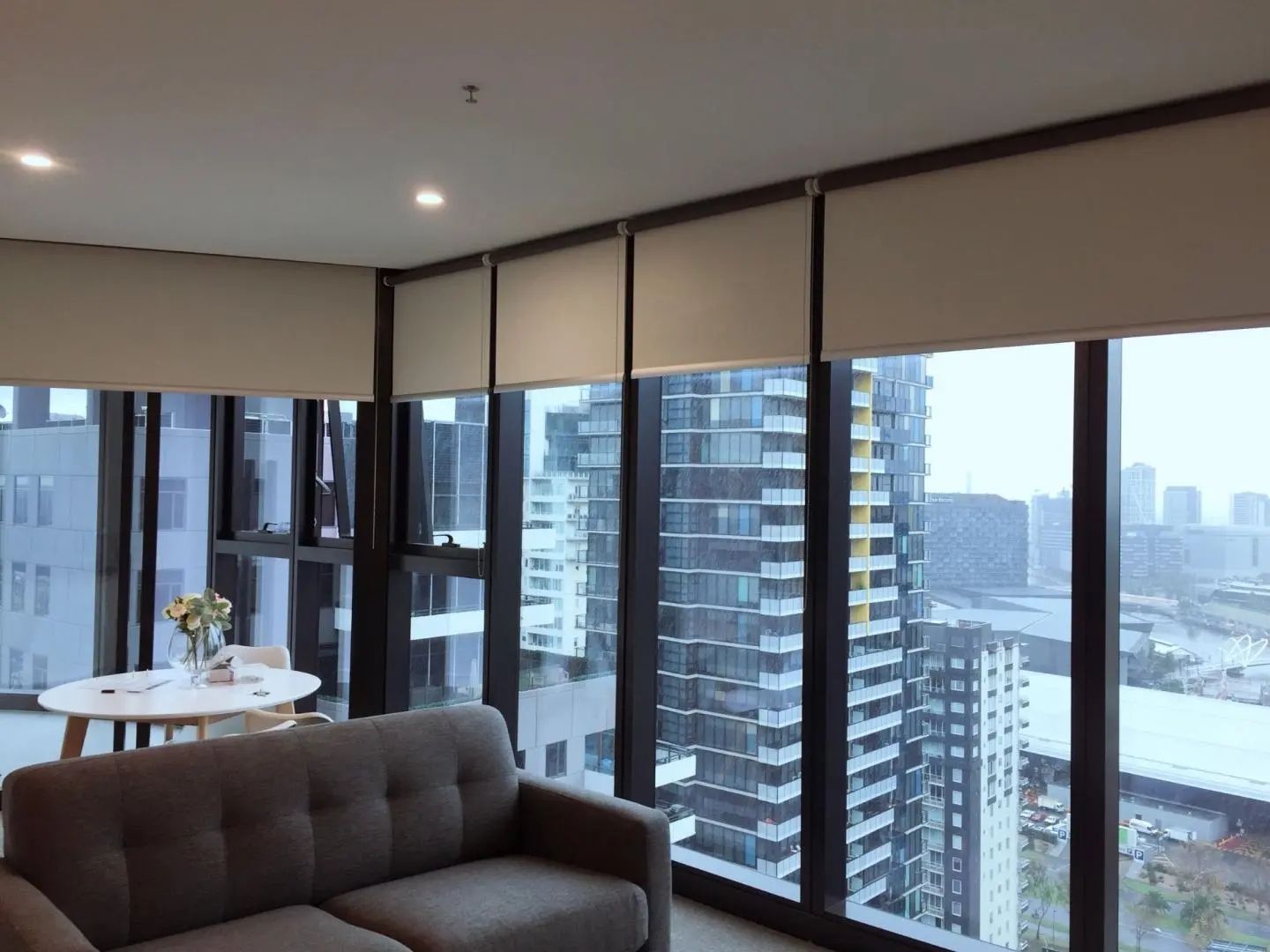 Modern apartment living room featuring roller blinds and a panoramic city view.