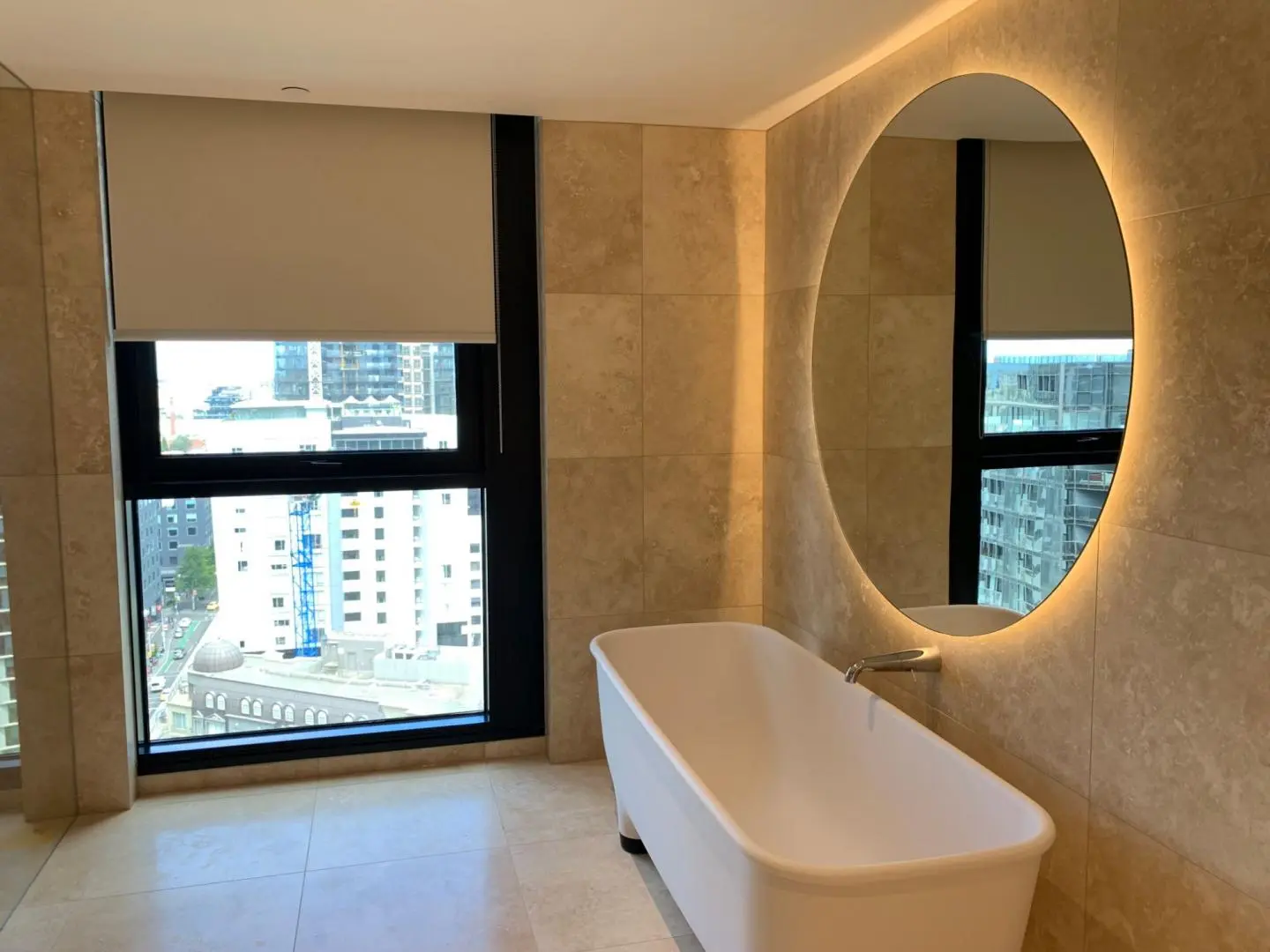 Luxurious modern bathroom featuring a freestanding tub, illuminated mirror, and urban views.