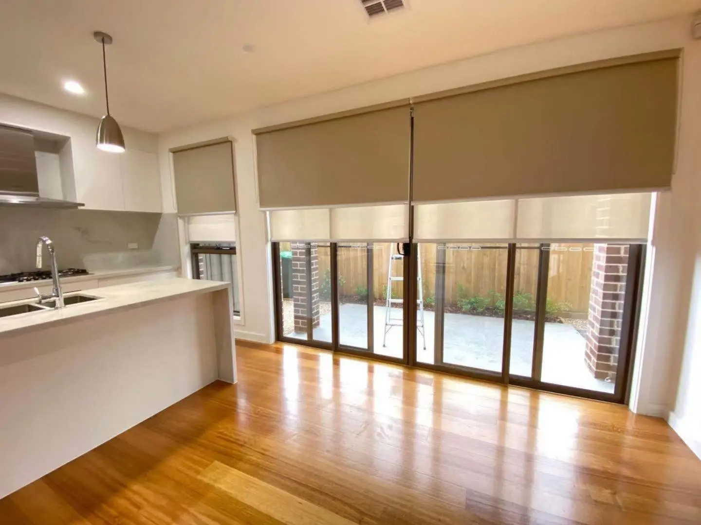 Modern kitchen and living room featuring dual roller blinds and hardwood floors.