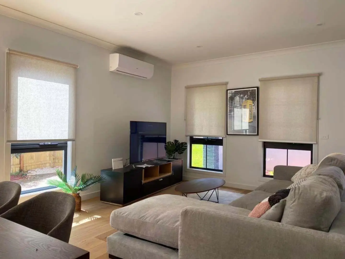 Modern living room interior with a large sectional sofa, TV, and roller blinds for controlled natural light.