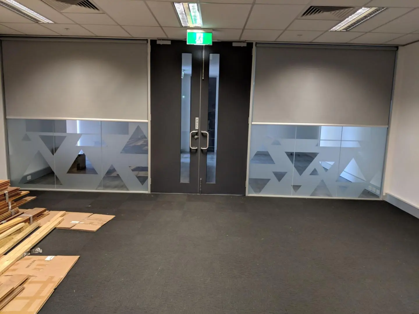 Empty modern office space with glass partitions, geometric privacy film, and gray roller blinds.