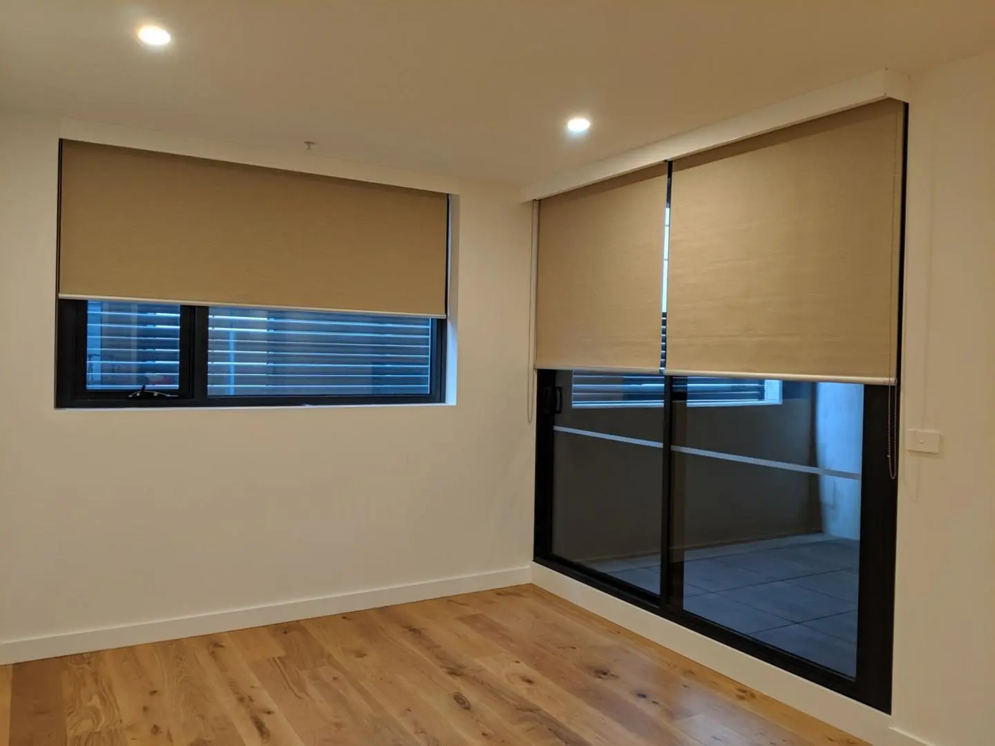 An empty room with tan roller shades on the windows.