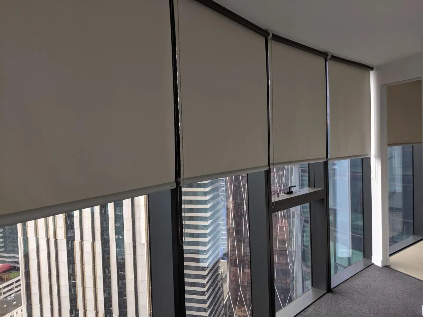 Tan roller blinds cover office windows with a city view.