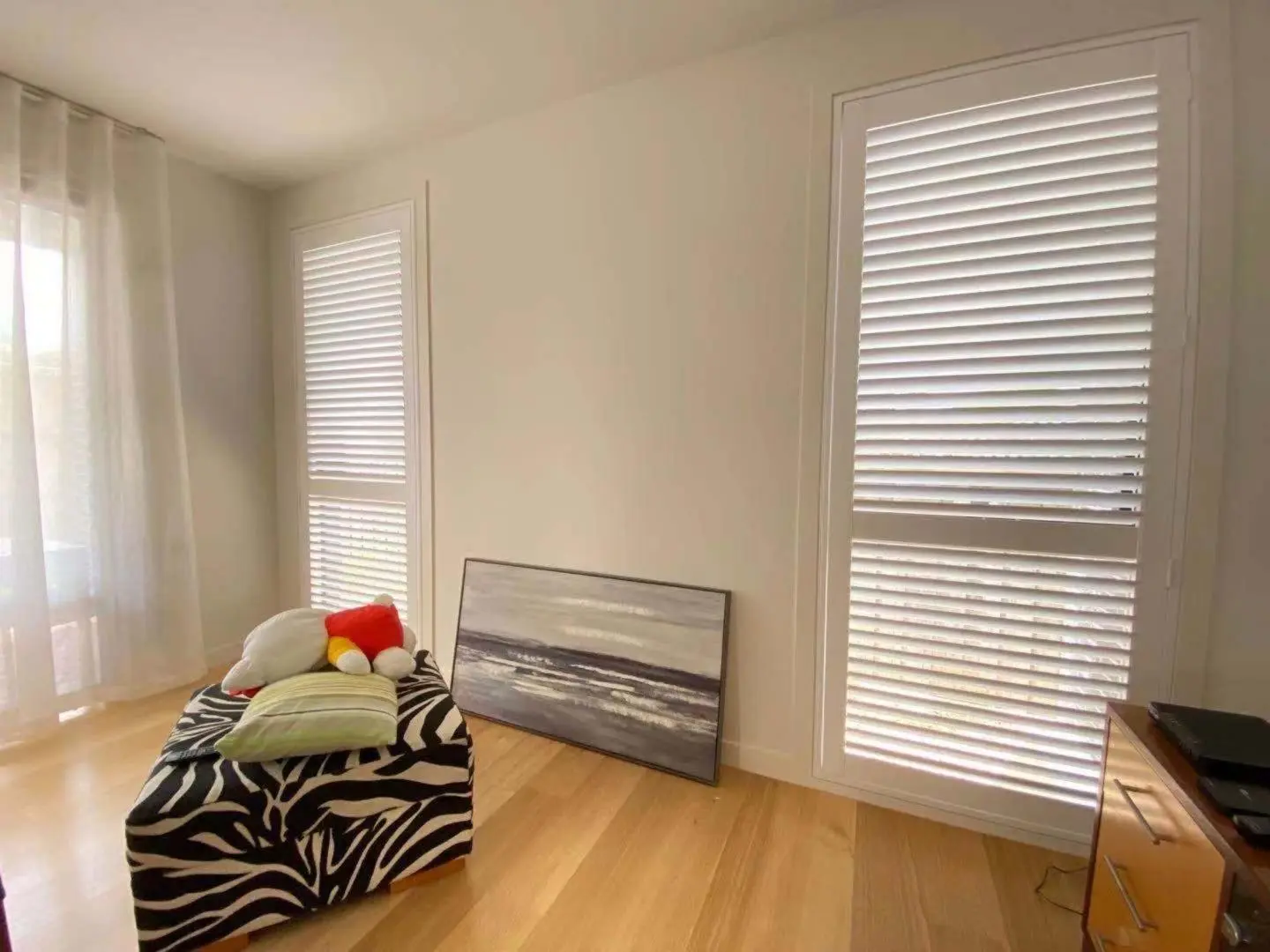 A bright living room showcases shuttered windows, a zebra-print ottoman, and abstract artwork.