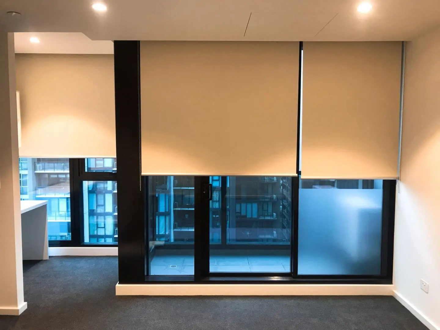 Spacious room with large windows fitted with neutral beige roller blinds.