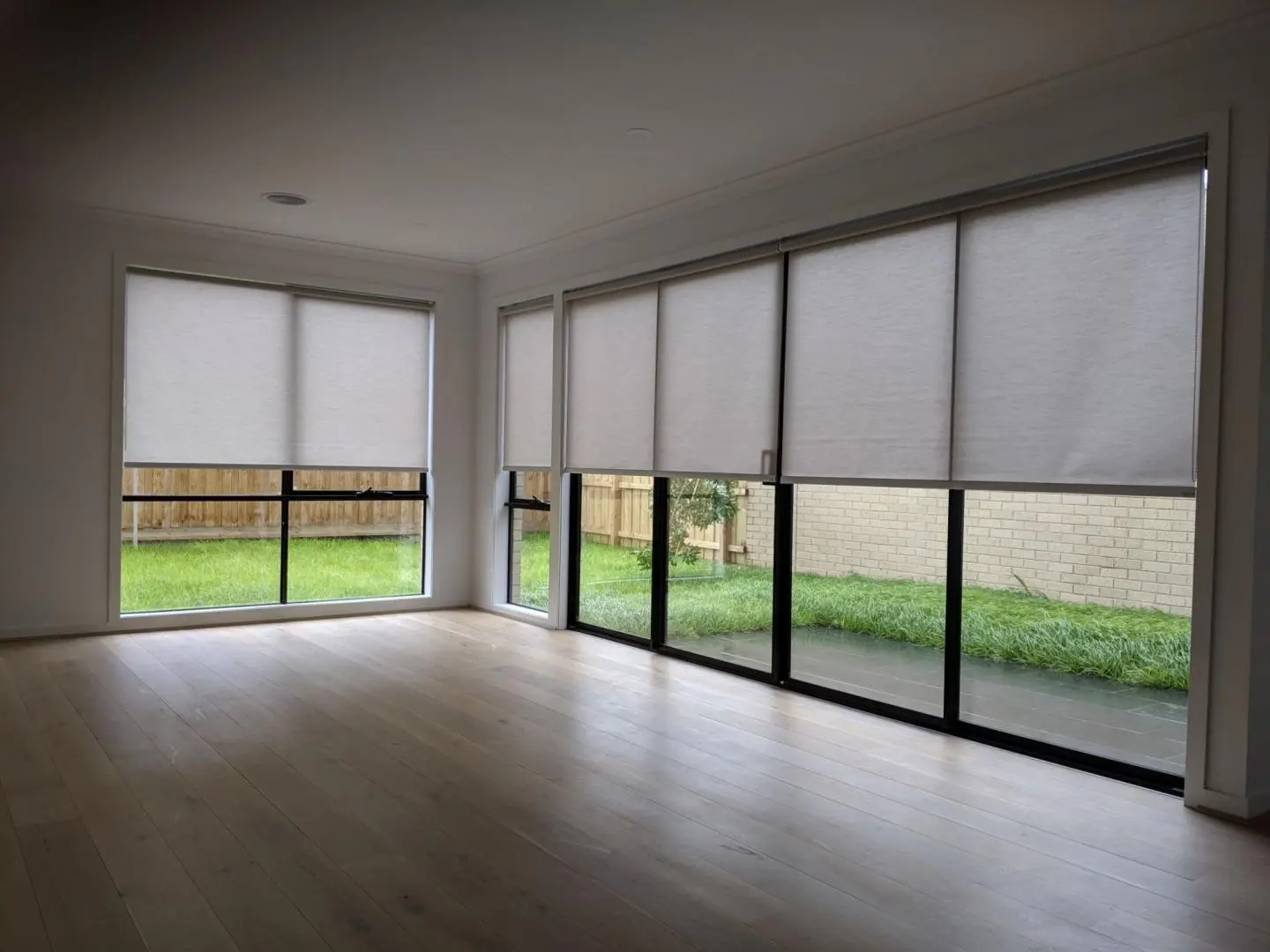 Modern roller blinds on large windows in a bright room with wooden floors.