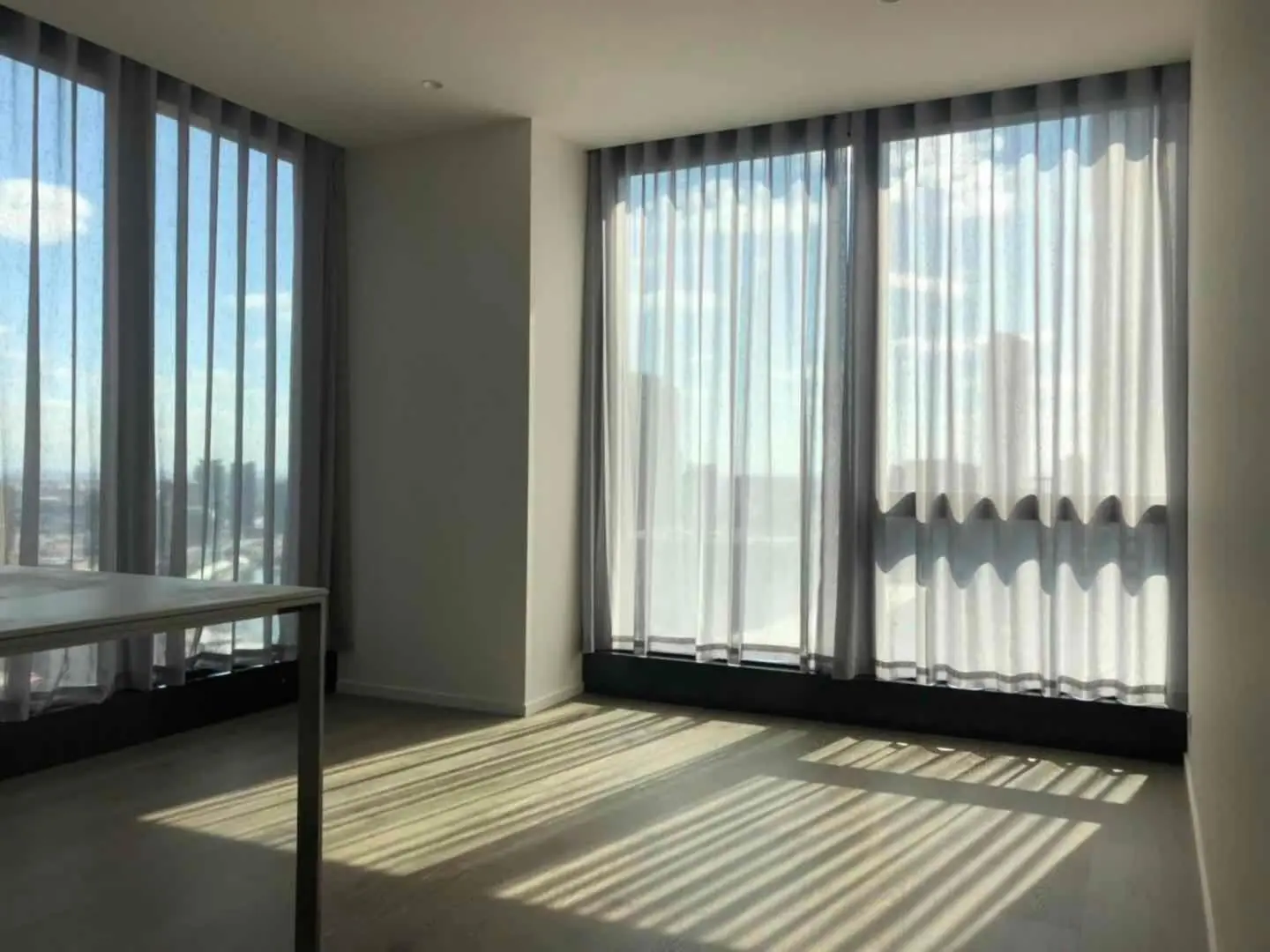 A sunlit room showcases sheer curtains, casting shadows on the wooden floor.