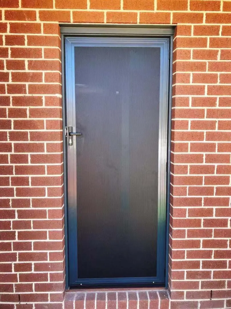A screen door offers security on a red brick wall.