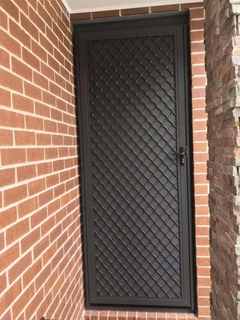 Secure your home with this durable steel mesh security door set against a brick wall.