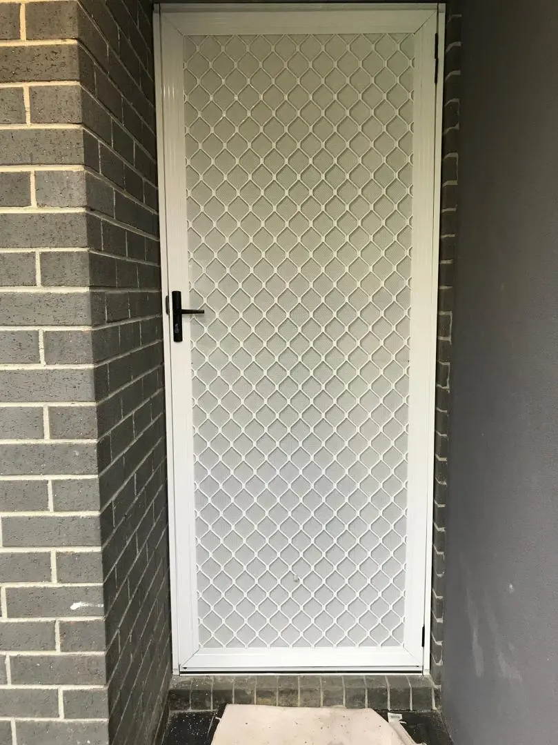 White security screen door with diamond mesh pattern in an exterior entryway.