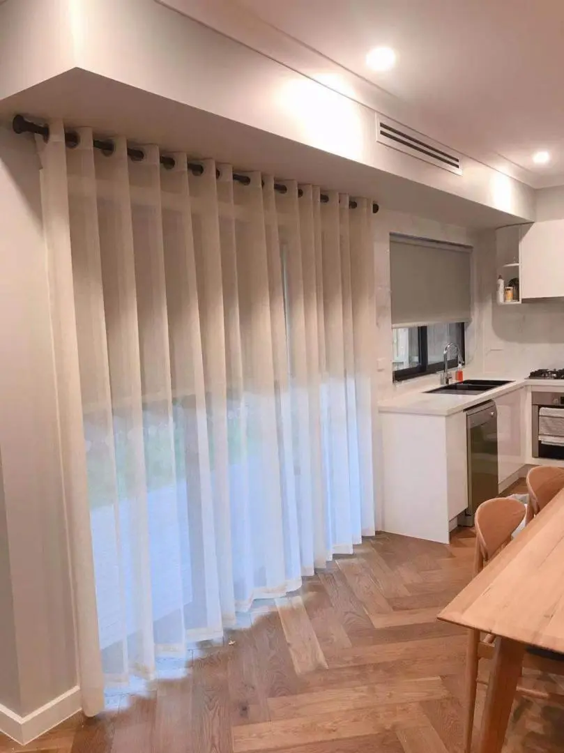 Modern sheer curtains frame a bright kitchen with white cabinets and herringbone wood floors.