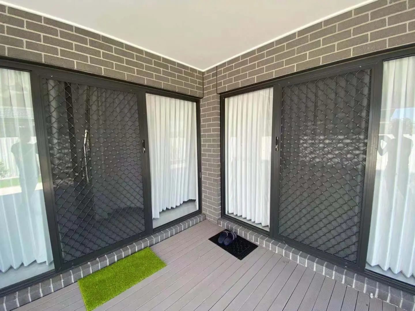 Sliding security screen doors lead to a patio with white curtains and a green doormat.