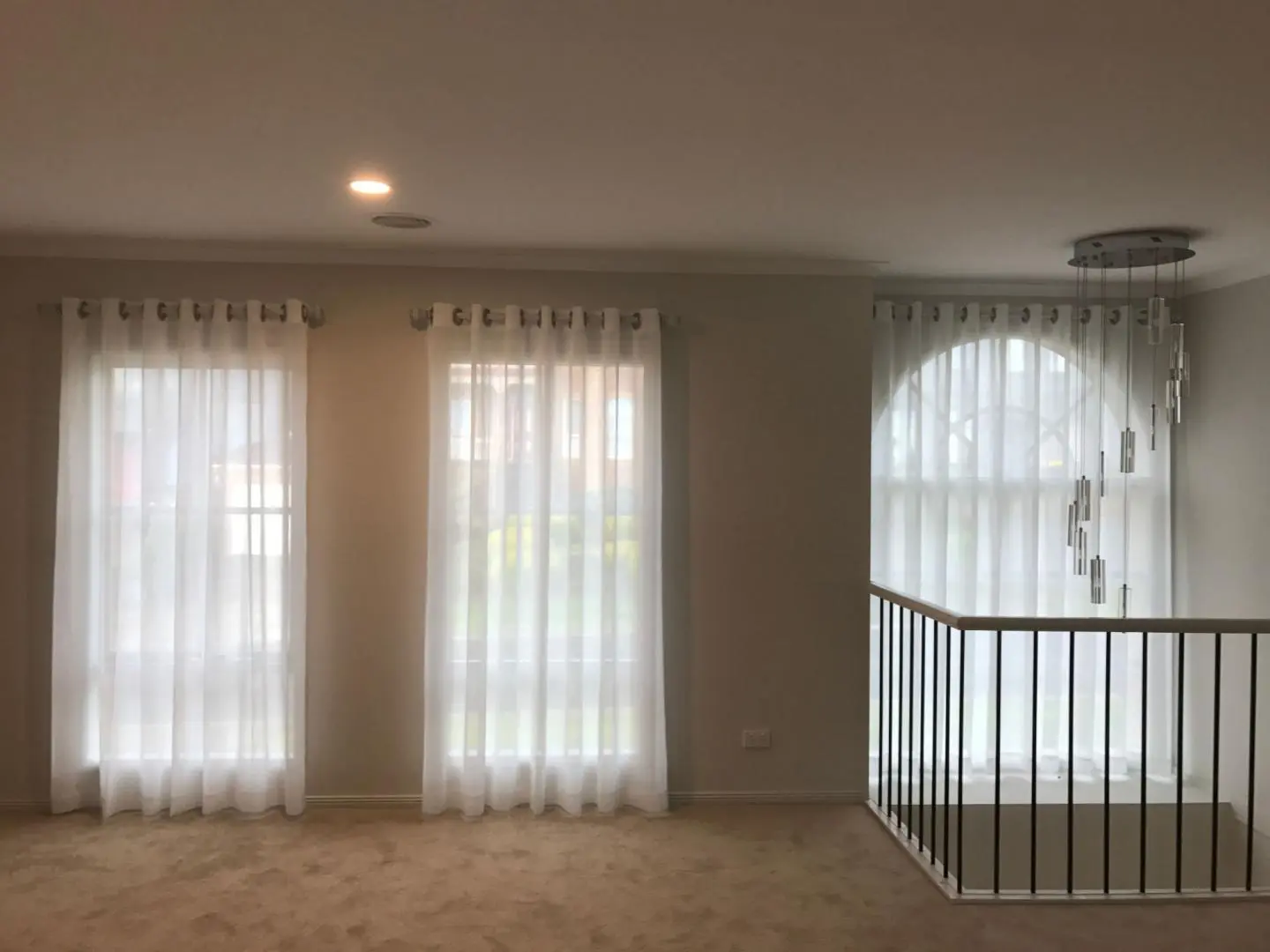 Elegant interior with white sheer curtains covering multiple windows and a modern chandelier.