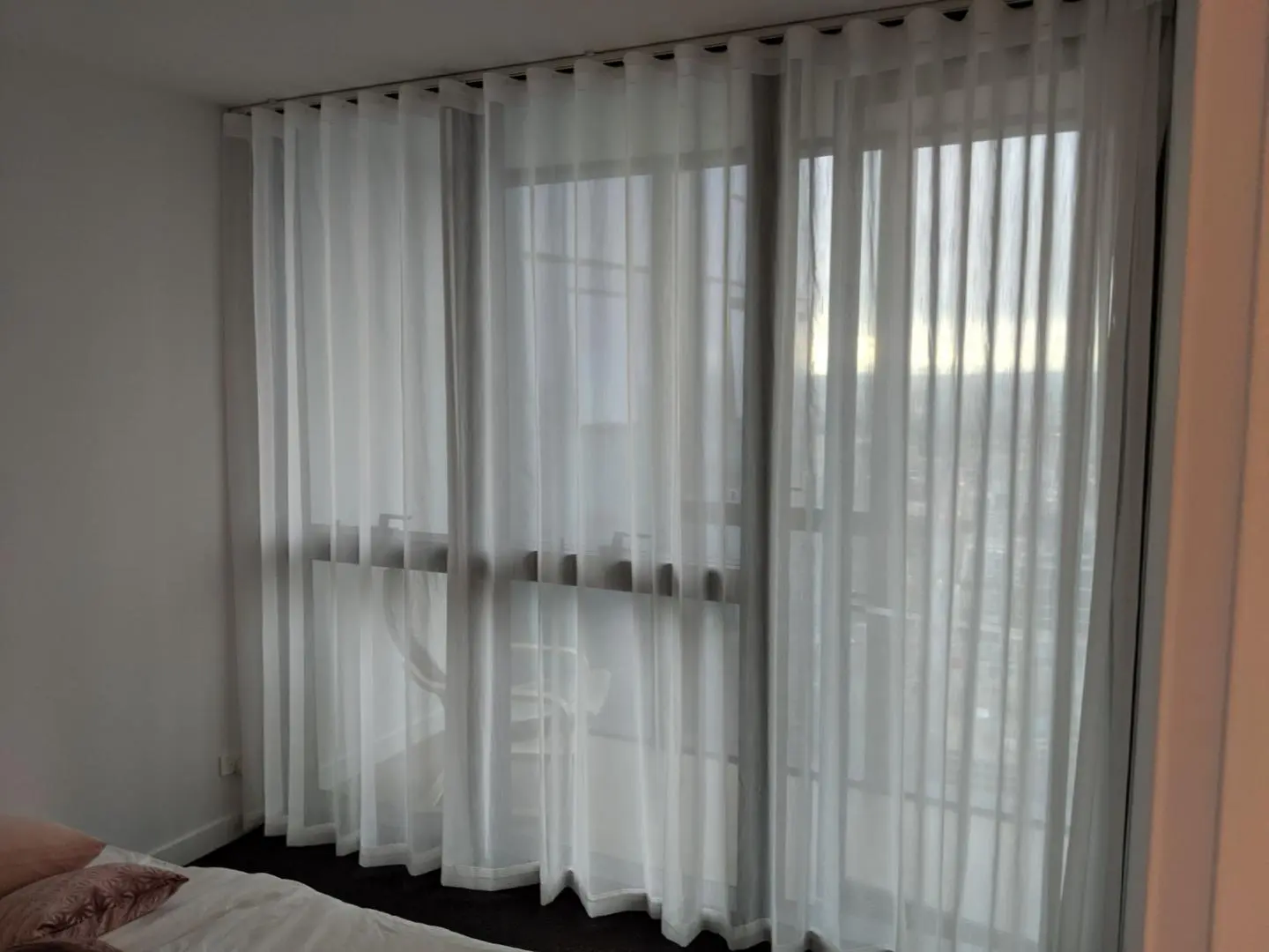 White sheer curtains beautifully filter natural light in a modern bedroom with a city view.