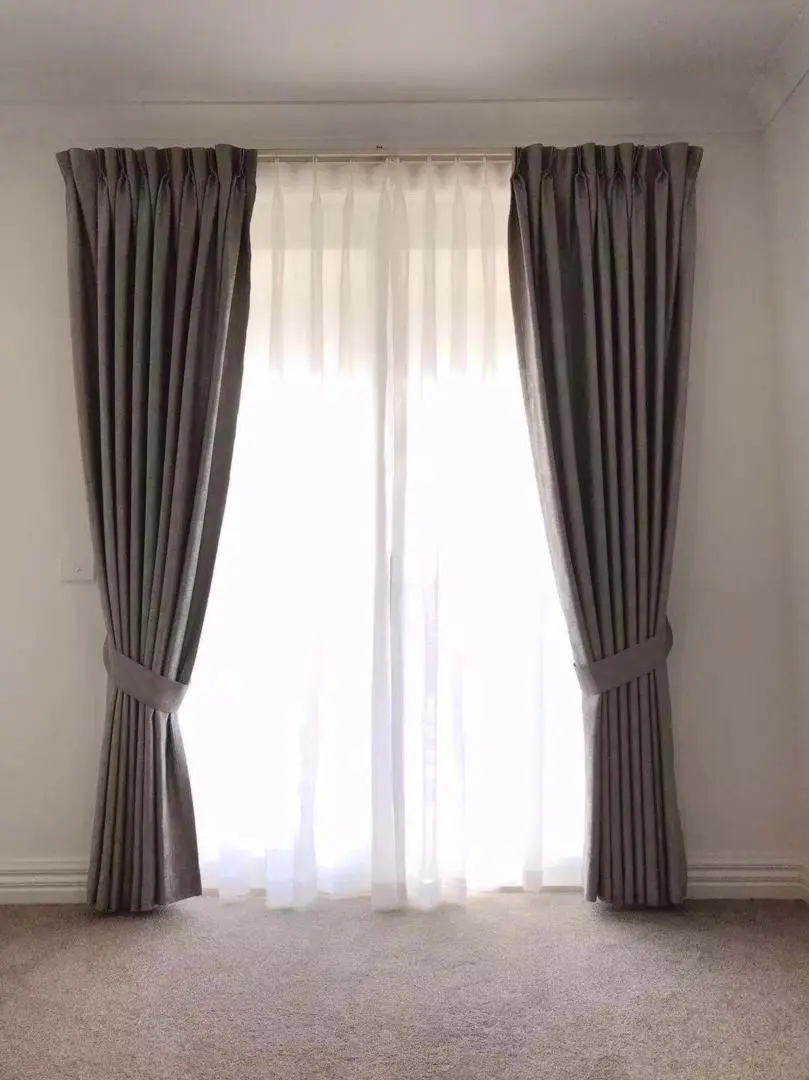 Gray curtains and sheer drapes frame a bright window in a carpeted room.