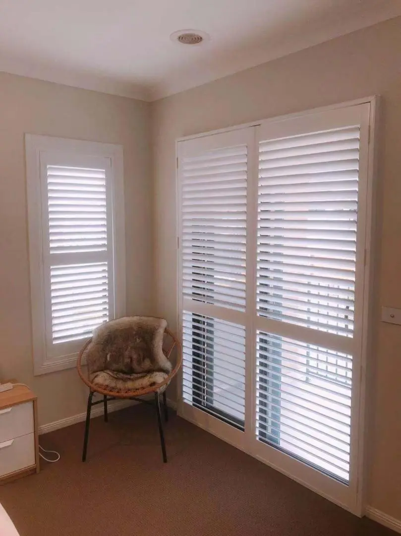 A cozy bedroom features white shutters, a comfortable chair, and a simple design.