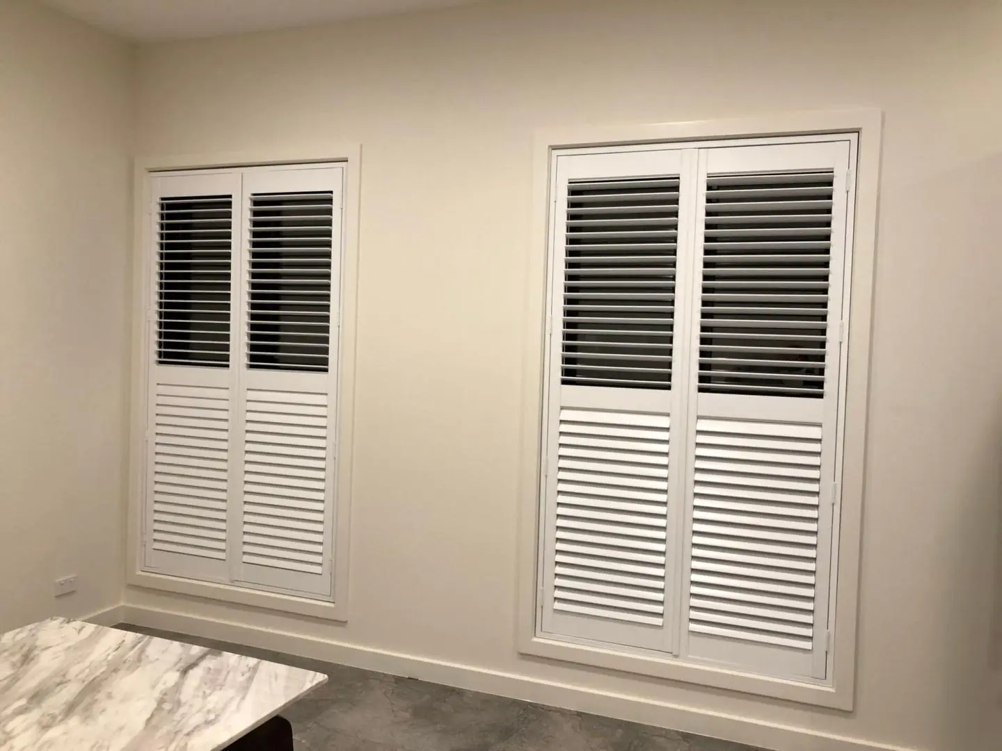 Bright white shutters adorn the windows in a neutral-toned room, offering a clean and stylish design.